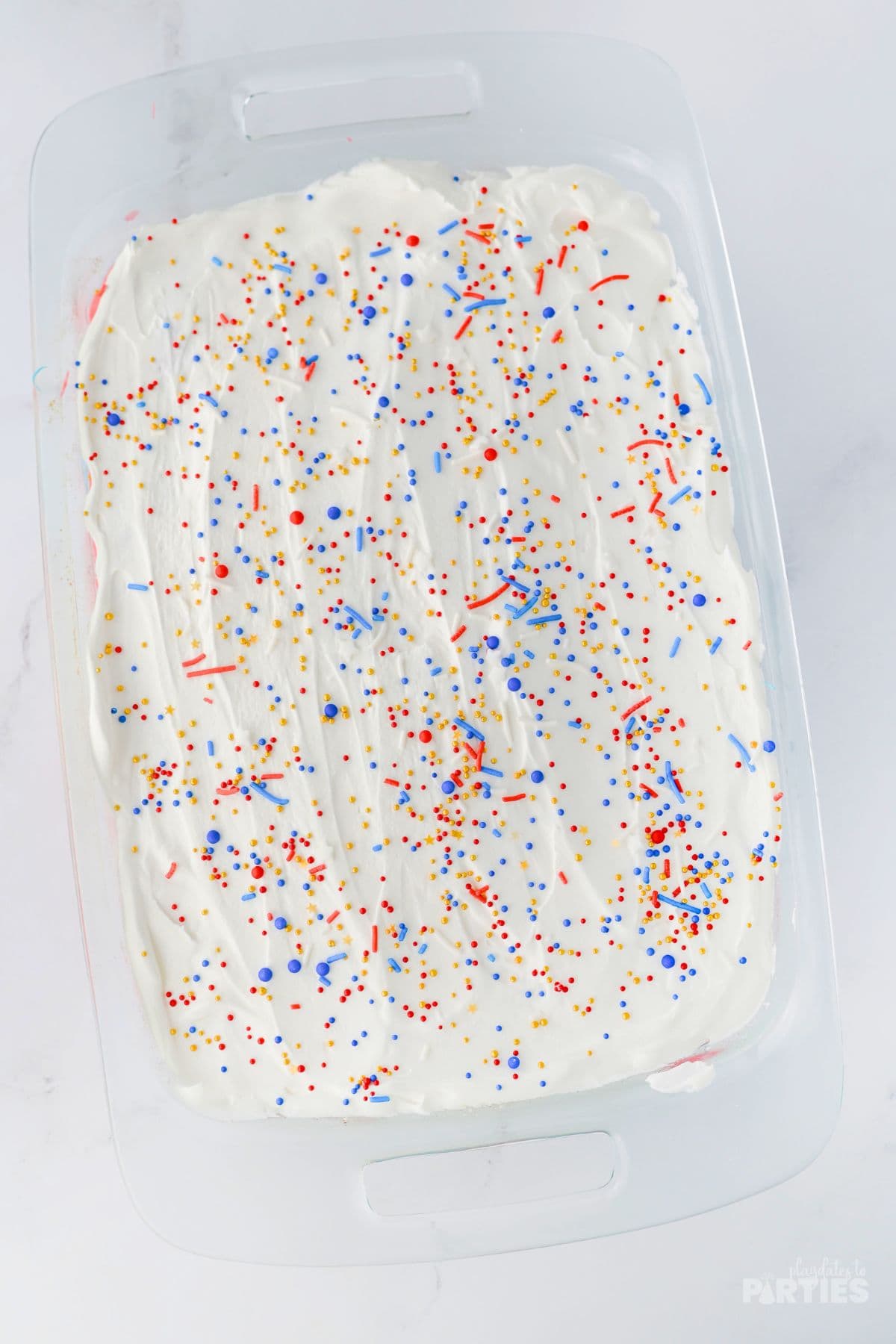 Red white and blue sprinkles on the top of a sheet cake.