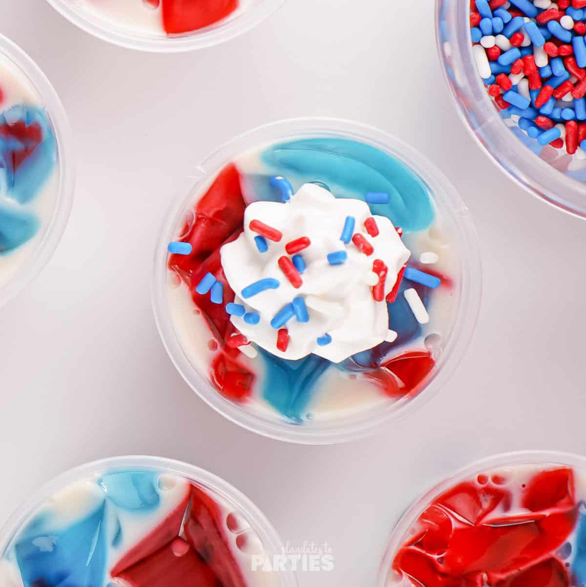 Whipped cream and patriotic sprinkles top off a cup of red white and blue stained glass jello.