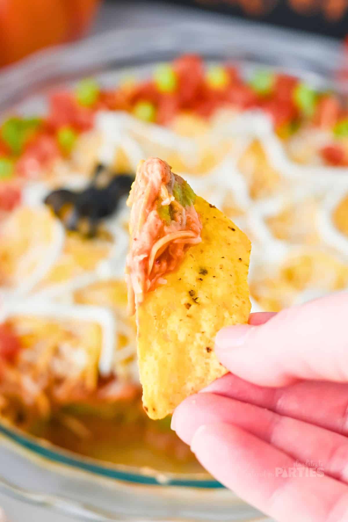 A woman's hand holding a chip with layered taco dip.