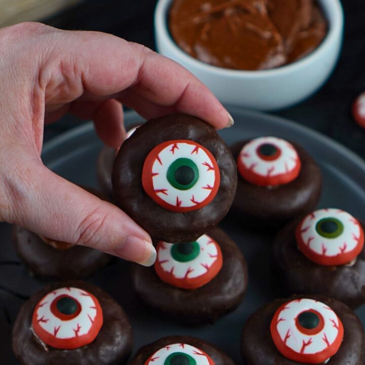A womans hand holding up a mini donut eyeball Halloween treat.