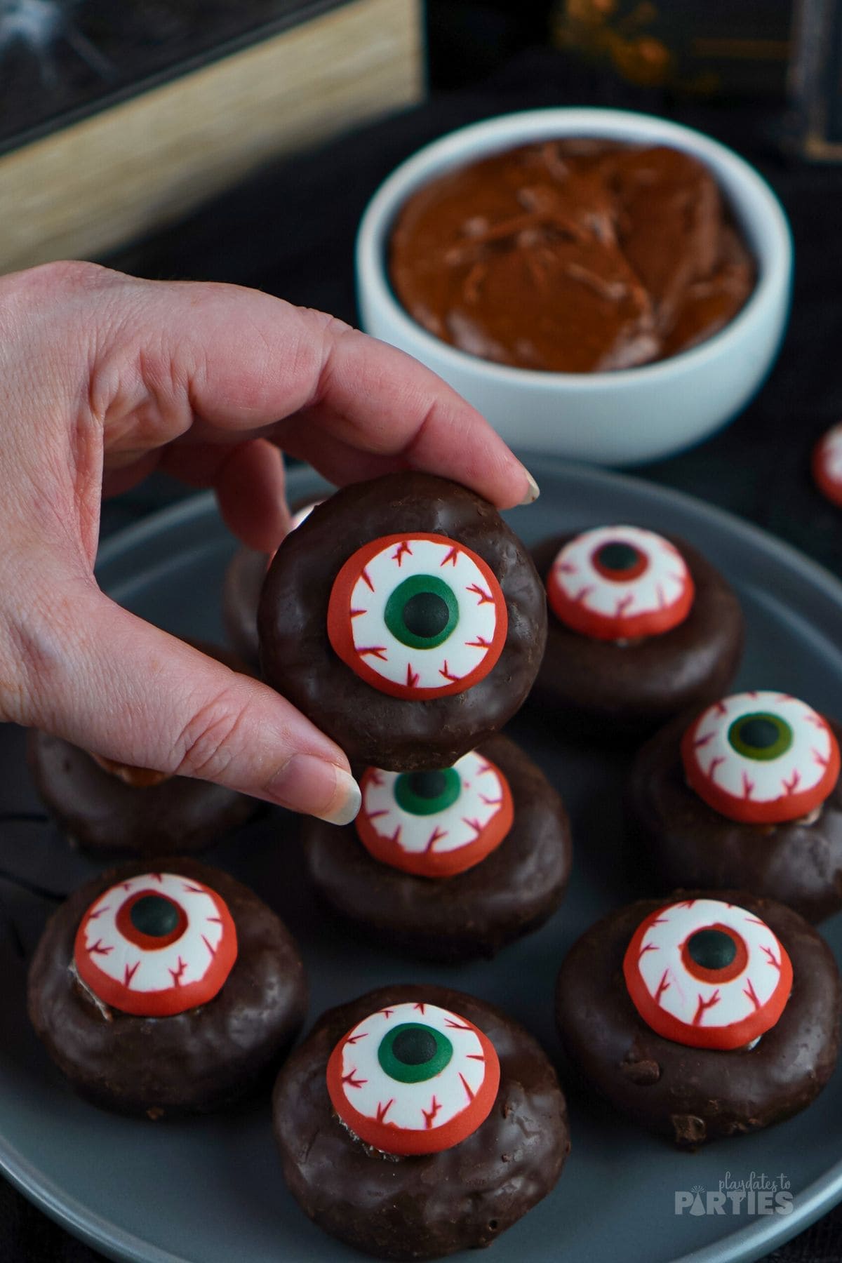 A womans hand holding up a mini donut eyeball Halloween treat.